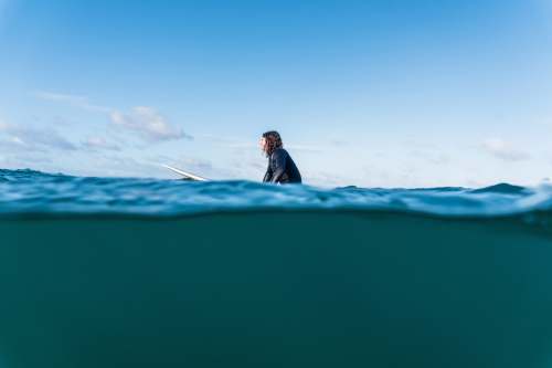 te arai man in black jacket sitting on blue surfboard during daytime new zealand